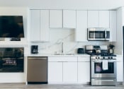 Thumbnail 24 of 29 - Kitchen with stainless steel dishwasher, gas range, micro hood microwave, single kitchen sink, backsplash and countertops, white kitchen cabinets, cozy fireplace on the left