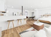Thumbnail 6 of 32 - A modern living room with a kitchen area in the background.