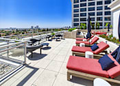 Thumbnail 52 of 56 - A patio with red cushioned seating and blue umbrellas overlooking a city skyline.