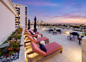 Thumbnail 56 of 56 - A patio with red cushioned chairs and umbrellas overlooking a cityscape at dusk.