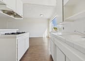 Thumbnail 21 of 33 - A white kitchen with wooden floors and a window.