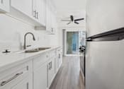 Thumbnail 12 of 33 - A modern kitchen with white cabinets and a wooden floor.