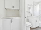 Thumbnail 19 of 33 - A white bathroom with a toilet, sink, and cabinets.