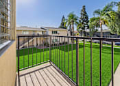 Thumbnail 52 of 75 - A balcony with a black railing overlooks a green lawn and a row of houses.