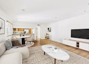 Thumbnail 7 of 24 - A living room with a white couch, a coffee table, and a television.