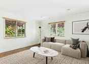 Thumbnail 6 of 24 - A living room with a grey couch, a white coffee table, and a painting on the wall.