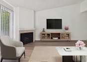 Thumbnail 5 of 45 - A living room with a fireplace, a chair, a table, and a television.