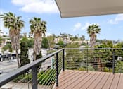 Thumbnail 89 of 119 - A balcony with a wooden floor and a metal railing with palm trees in the background.