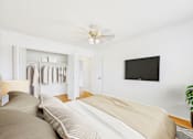 Thumbnail 2 of 19 - A bedroom with a bed, a plant, and a flat screen TV mounted on the wall.