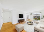 Thumbnail 3 of 19 - A living room with a white couch, a white chair, a white ottoman, a black television, a wooden floor, and a white wall.