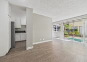 Thumbnail 38 of 51 - A spacious kitchen with white cabinets and a refrigerator is adjacent to a living room with a sliding glass door leading to a balcony.