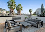 Thumbnail 23 of 119 - A patio with a couch, chairs, and a table with a view of palm trees and buildings.