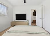 Thumbnail 9 of 28 - A bedroom with a bed, a television, and a window with blinds.
