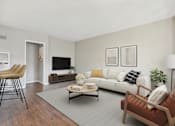 Thumbnail 12 of 32 - A living room with a white couch, a brown chair, and a grey rug.