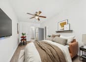 Thumbnail 6 of 19 - A bedroom with a bed, a ceiling fan, and a television.