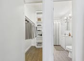 Thumbnail 7 of 19 - A white bathroom with a toilet, sink, and a closet with a grey robe hanging.