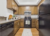 Thumbnail 1 of 46 - A black refrigerator stands in a kitchen with wooden cabinets and a black oven.