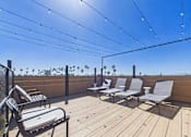 Thumbnail 27 of 33 - A wooden deck with chairs and a table is covered with string lights.