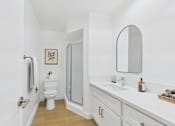 Thumbnail 9 of 19 - A white bathroom with a toilet, sink, mirror, and shower.