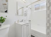 Thumbnail 22 of 30 - A white bathroom with a sink, mirror, and bathtub.