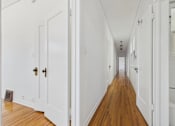 Thumbnail 12 of 23 - A long hallway with white walls and wood floors.