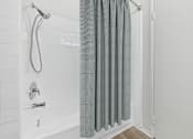 Thumbnail 14 of 108 - A white tiled bathroom with a shower and a grey curtain.