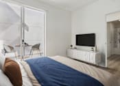 Thumbnail 18 of 61 - A bedroom with a bed, a chair, a television, and a window.