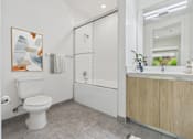 Thumbnail 10 of 45 - A white toilet is in a bathroom with a white tub and a wooden cabinet.