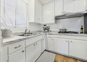 Thumbnail 3 of 36 - A white kitchen with a sink, stove, and cabinets.