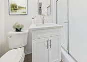 Thumbnail 6 of 12 - A white bathroom with a toilet, sink, and a framed picture on the wall.