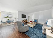 Thumbnail 2 of 29 - A living room with a grey sofa, a grey armchair, a wooden coffee table, and a flat screen TV mounted on the wall.