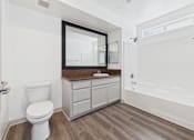 Thumbnail 10 of 35 - A white toilet sits in a bathroom with a wooden floor and white walls.