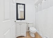 Thumbnail 12 of 15 - A white bathroom with a toilet and a mirror.