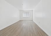 Thumbnail 11 of 15 - A room with wooden flooring and a white wall with a vent.