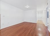 Thumbnail 6 of 15 - A long empty room with wooden floors and white walls.