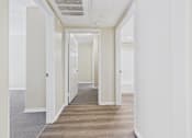 Thumbnail 24 of 30 - A long hallway with white walls and a carpeted floor.