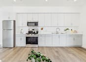 Thumbnail 9 of 13 - A modern kitchen with white cabinets and a wooden floor.
