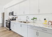 Thumbnail 8 of 13 - A modern kitchen with white cabinets and a marble countertop.