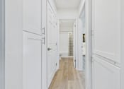 Thumbnail 8 of 73 - A long hallway with white doors and wood floors.