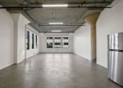 Thumbnail 21 of 92 - A large empty room with a curved concrete ceiling and a stainless steel refrigerator on the right side.