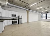 Thumbnail 8 of 92 - A large empty room with a kitchen area to the left.
