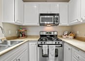 Thumbnail 1 of 26 - A kitchen with white cabinets and a black microwave above the stove.