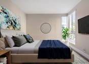 Thumbnail 5 of 26 - A bedroom with a bed, a painting, a plant, and a television.
