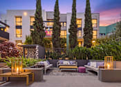 Thumbnail 27 of 40 - A modern outdoor seating area with a fire pit and cushioned benches.