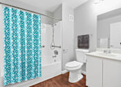 Thumbnail 12 of 40 - a bathroom with a white toilet next to a bathtub with a blue shower curtain