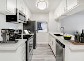 Thumbnail 1 of 24 - A modern kitchen with a refrigerator, microwave, and coffee maker.