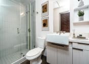 Thumbnail 13 of 45 - Apartments For Rent In Downtown Los Angeles, CA - Broadway Lofts - Bathroom With A Large Vanity Mirror, Sink, Wood-Grain Like Cabinets, A Toilet, Tile Backsplash, And A Shower With Tub