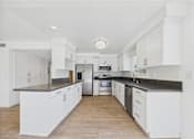 Thumbnail 105 of 135 - A kitchen with white cabinets and black countertops.