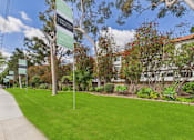 Thumbnail 12 of 64 - A green sign with white text on a pole in front of a tree.
