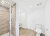 Thumbnail 22 of 22 - A white toilet sits in a bathroom with a walk-in shower.